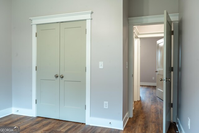 unfurnished bedroom with a closet, baseboards, and dark wood-type flooring