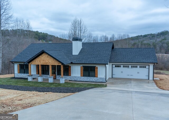modern inspired farmhouse with a garage, covered porch, roof with shingles, a chimney, and concrete driveway