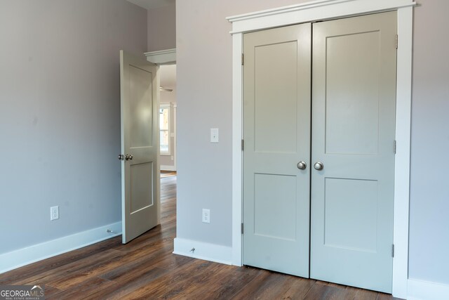 unfurnished bedroom featuring a closet, baseboards, and dark wood-type flooring