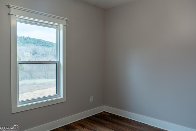 unfurnished room featuring baseboards and dark wood-type flooring
