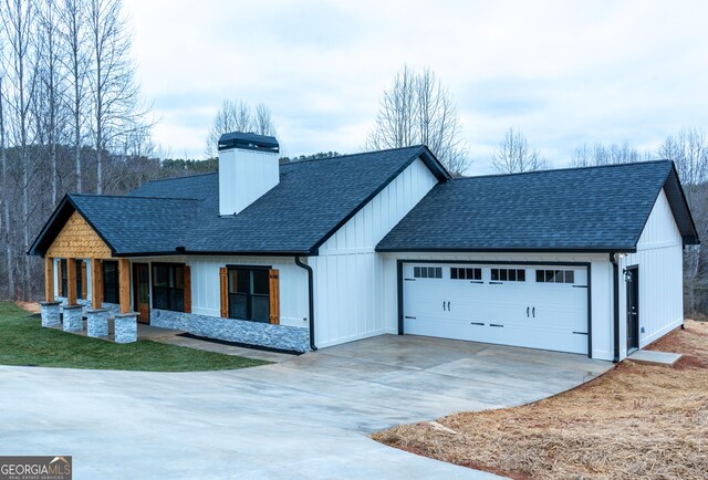 modern inspired farmhouse featuring roof with shingles, an attached garage, stone siding, a chimney, and concrete driveway