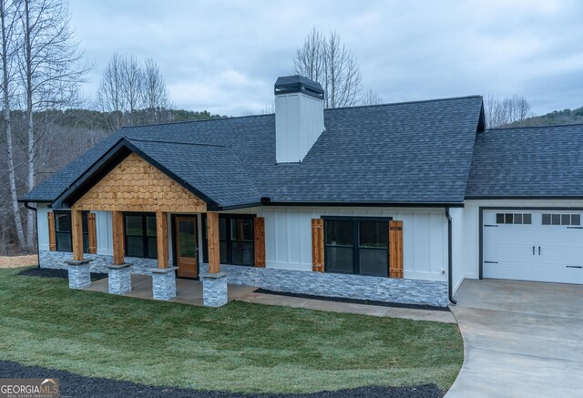 rear view of house with an attached garage, a shingled roof, driveway, and a chimney