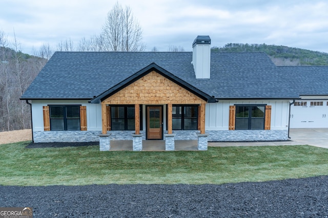 view of front of home with board and batten siding, a chimney, a front yard, an attached garage, and a shingled roof