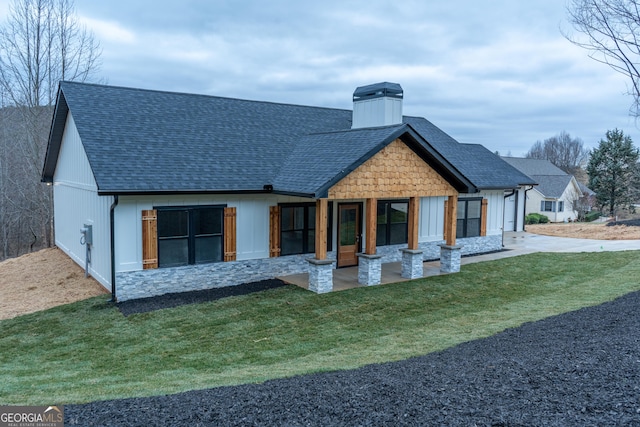 rear view of house featuring a shingled roof and a yard