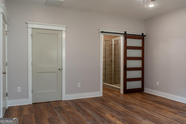 unfurnished bedroom featuring connected bathroom, baseboards, dark wood-style floors, and a barn door
