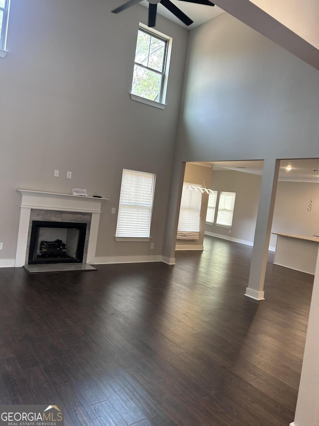 unfurnished living room with a high end fireplace, a towering ceiling, dark wood-style floors, and ceiling fan