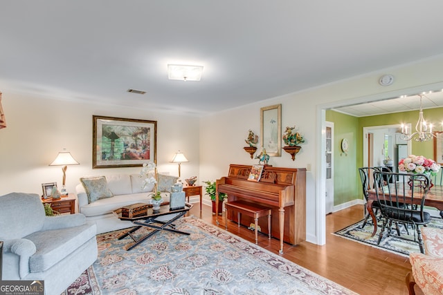 living area featuring visible vents, wood finished floors, baseboards, an inviting chandelier, and ornamental molding