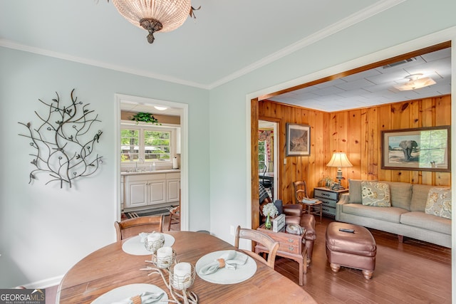 dining space featuring crown molding, wood finished floors, wooden walls, and visible vents