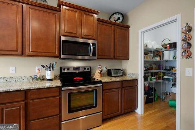 kitchen featuring brown cabinets, stainless steel appliances, light stone counters, and light wood-style floors