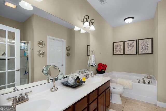 full bathroom featuring double vanity, tile patterned flooring, a sink, and a garden tub