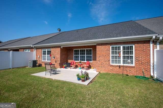 back of property featuring fence, brick siding, central air condition unit, a patio, and a yard