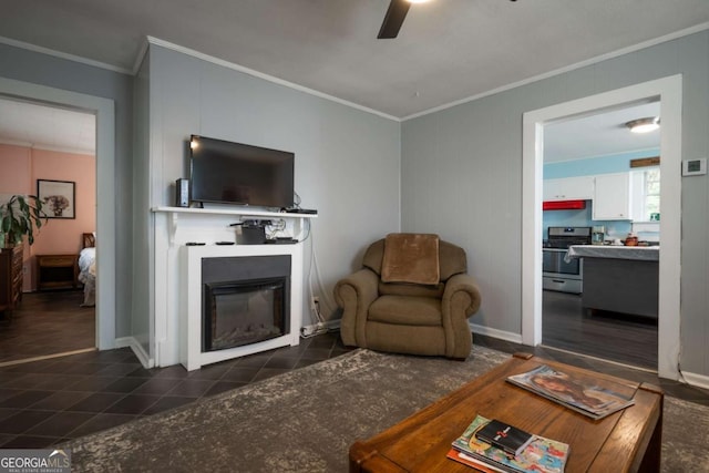 living room with crown molding, a ceiling fan, a glass covered fireplace, and dark tile patterned floors