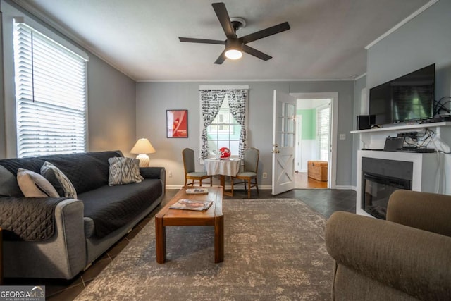 living area with ornamental molding, a glass covered fireplace, baseboards, tile patterned floors, and a ceiling fan