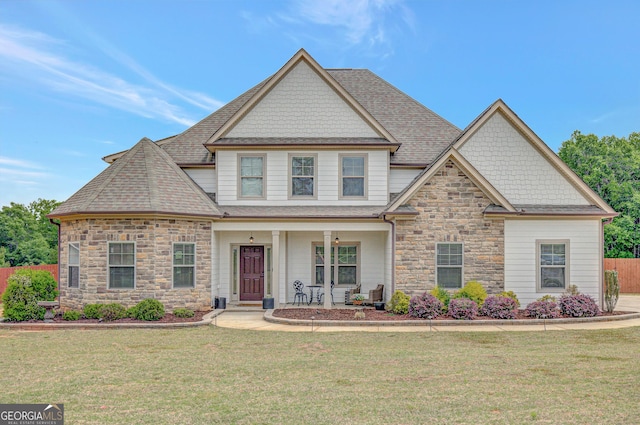craftsman-style home featuring a front lawn, fence, stone siding, a shingled roof, and a porch
