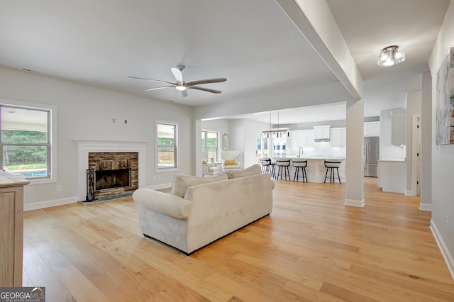 living room with a stone fireplace, plenty of natural light, light wood finished floors, and ceiling fan