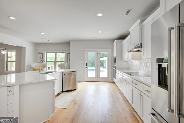 kitchen featuring visible vents, a sink, light wood finished floors, under cabinet range hood, and stainless steel appliances