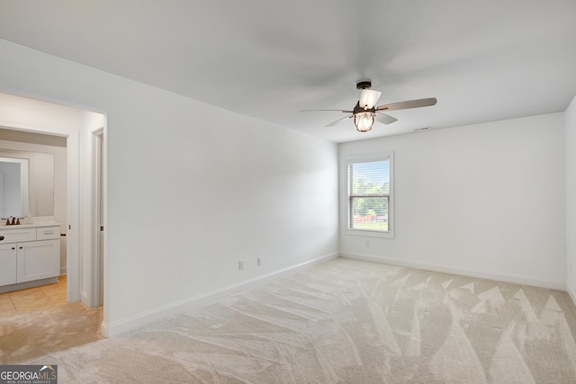 unfurnished room with visible vents, a sink, baseboards, light colored carpet, and a ceiling fan