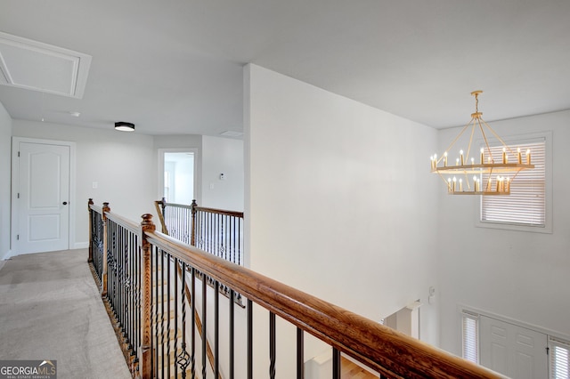 corridor featuring attic access, an upstairs landing, baseboards, a notable chandelier, and light carpet