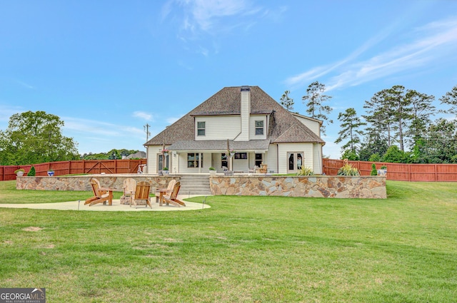 back of house with roof with shingles, a lawn, a patio area, a fenced backyard, and an outdoor fire pit
