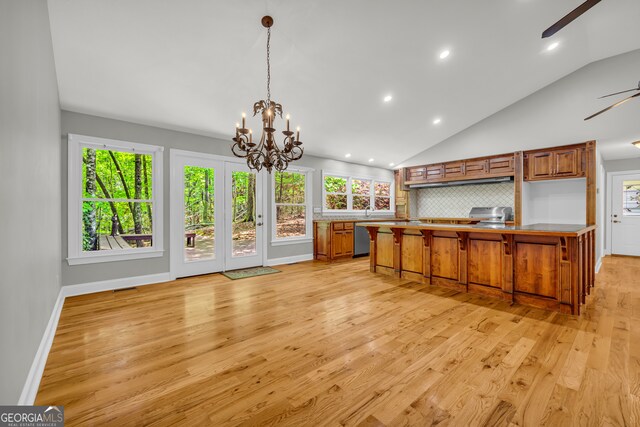 kitchen with brown cabinetry, ceiling fan with notable chandelier, light wood-type flooring, and backsplash