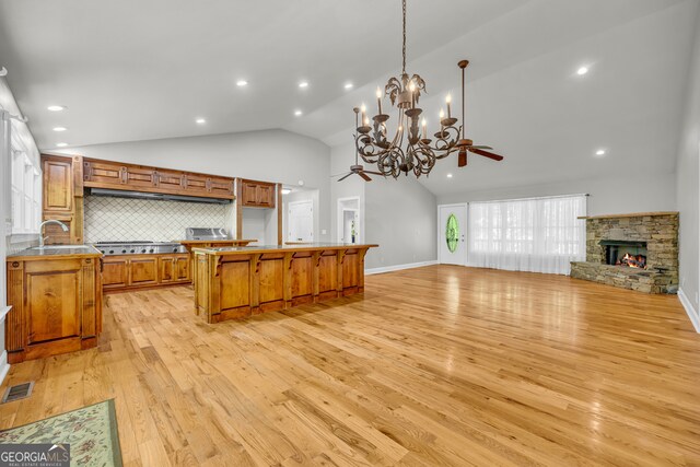 kitchen featuring brown cabinetry, a stone fireplace, tasteful backsplash, ceiling fan with notable chandelier, and open floor plan