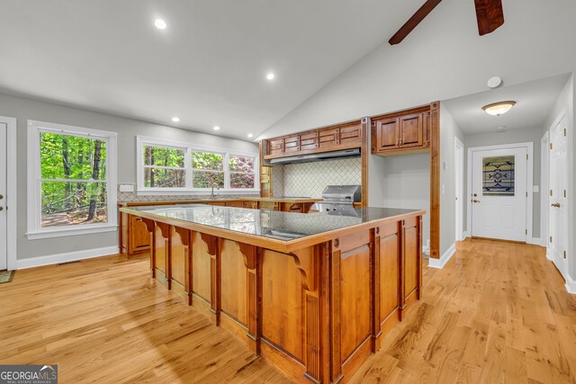 kitchen featuring light wood-style floors, recessed lighting, under cabinet range hood, brown cabinets, and backsplash