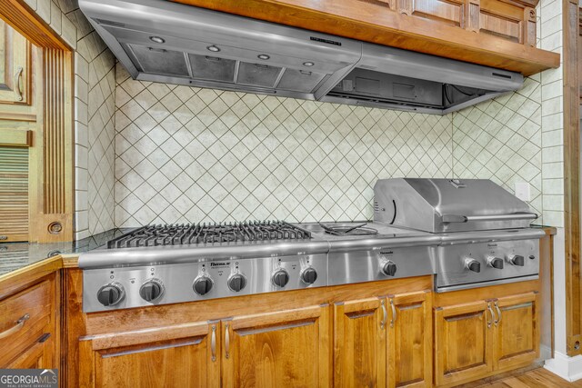 kitchen with brown cabinets, under cabinet range hood, tasteful backsplash, and stainless steel gas stovetop