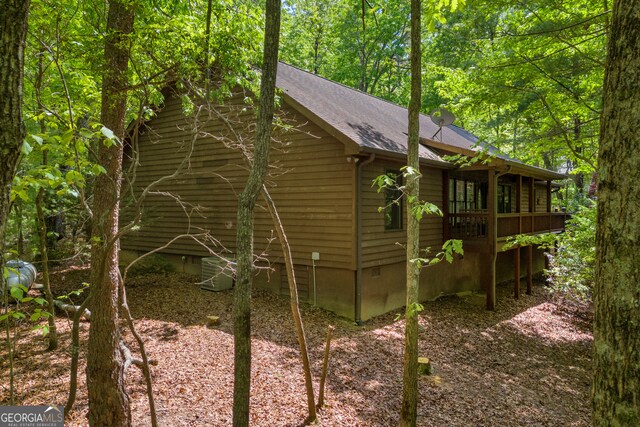 view of property exterior featuring central air condition unit, a forest view, and roof with shingles