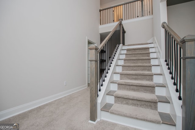 staircase featuring carpet floors, baseboards, and a high ceiling
