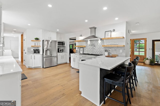 kitchen featuring high quality appliances, tasteful backsplash, open shelves, a peninsula, and wall chimney exhaust hood