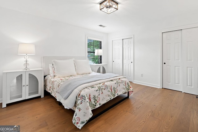 bedroom with baseboards, multiple closets, wood finished floors, and visible vents