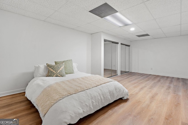 bedroom featuring multiple closets, baseboards, wood finished floors, and a paneled ceiling