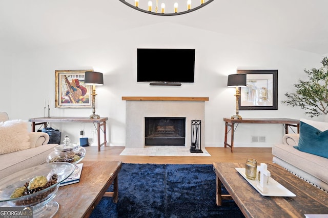 living room with visible vents, a fireplace with flush hearth, vaulted ceiling, wood finished floors, and baseboards