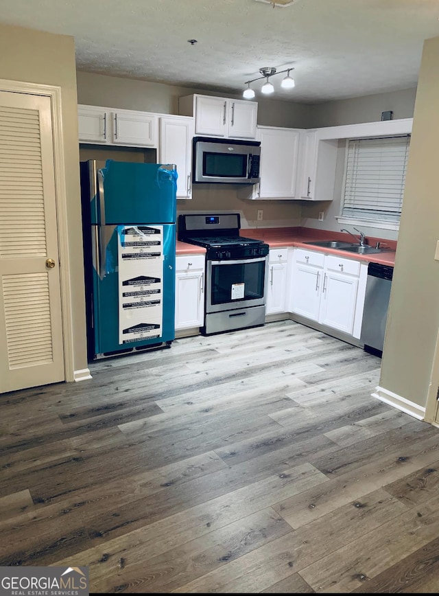 2353 Wellington Cir, Lithonia, GA 30058 - kitchen featuring white cabinets, a sink, stainless steel appliances, baseboards, and wood finished floors