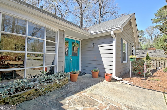 view of exterior entry with a shingled roof and fence
