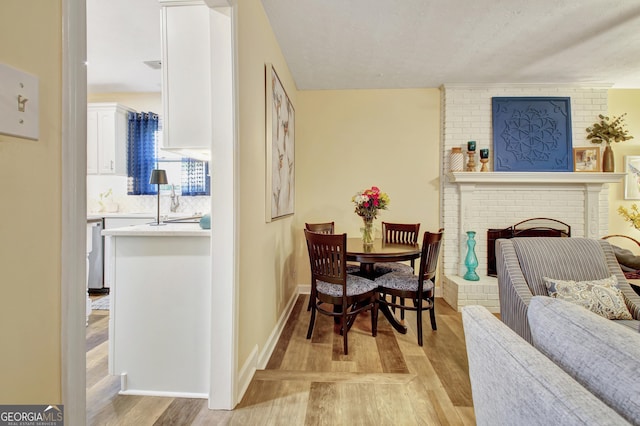dining area with baseboards, a brick fireplace, and light wood-type flooring