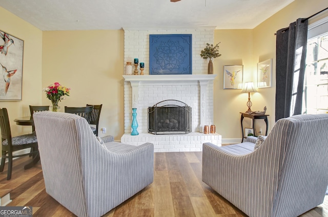 living room with a brick fireplace, ceiling fan, and wood finished floors