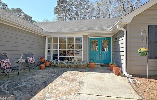 doorway to property featuring a patio and roof with shingles