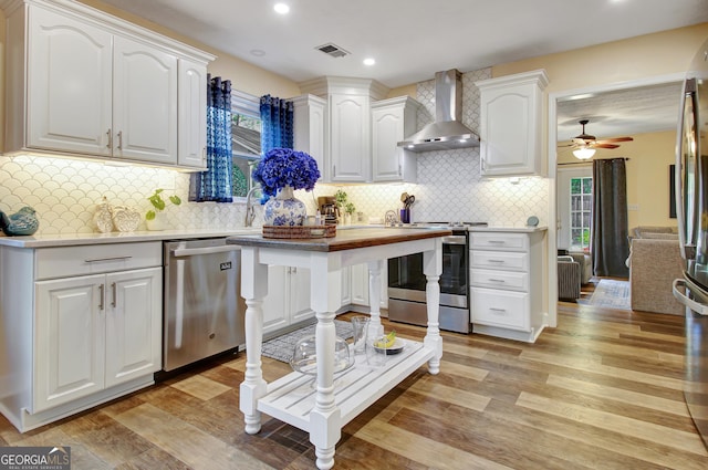 kitchen featuring wall chimney range hood, light countertops, white cabinets, and stainless steel appliances