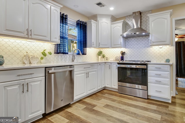 kitchen with visible vents, appliances with stainless steel finishes, light wood-type flooring, white cabinets, and wall chimney exhaust hood