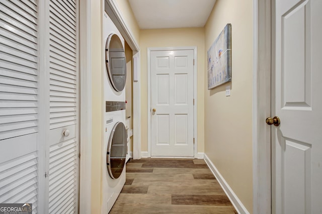 laundry room featuring baseboards, stacked washer / drying machine, wood finished floors, and laundry area