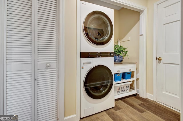 laundry area featuring baseboards, stacked washer / drying machine, wood finished floors, and laundry area
