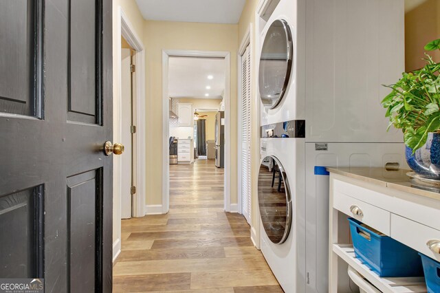 laundry room with laundry area, baseboards, light wood-style flooring, and stacked washer / drying machine