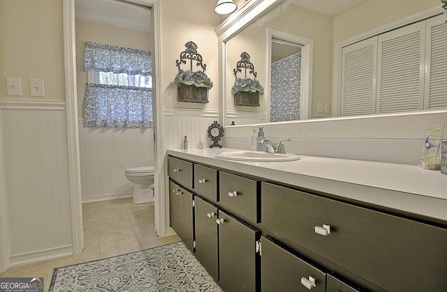 bathroom with toilet, wainscoting, tile patterned flooring, and vanity