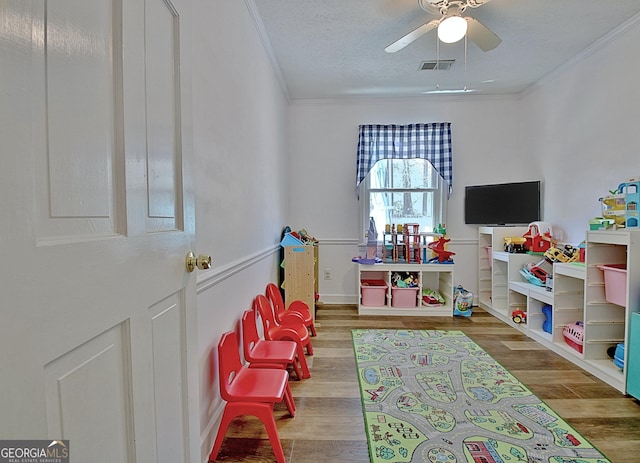 rec room with crown molding, ceiling fan, wood finished floors, and visible vents