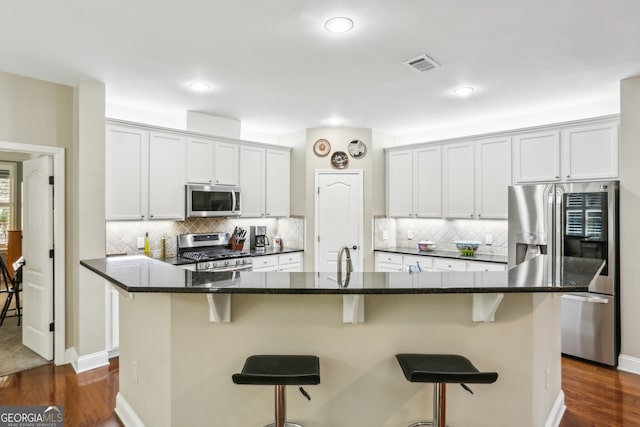 kitchen featuring visible vents, decorative backsplash, appliances with stainless steel finishes, and a breakfast bar area