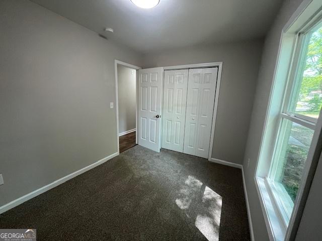 unfurnished bedroom with baseboards, a closet, and dark colored carpet
