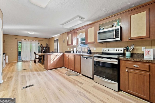 kitchen with stainless steel appliances, brown cabinetry, light wood finished floors, and a peninsula