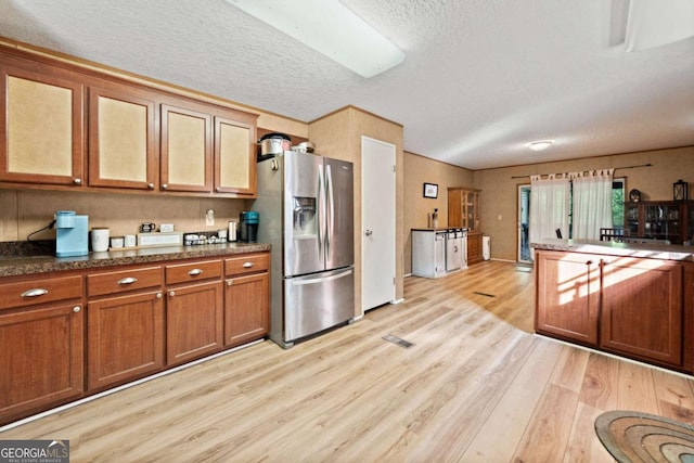 kitchen with glass insert cabinets, stainless steel fridge, a textured ceiling, brown cabinets, and light wood finished floors