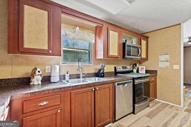 kitchen with brown cabinets, dark countertops, appliances with stainless steel finishes, a sink, and light wood-style floors